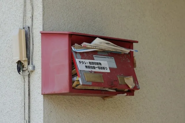 ポストに郵便物が溜まっているイメージ